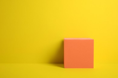 Photo of Orange cube on yellow background, space for text. Stylish presentation for product