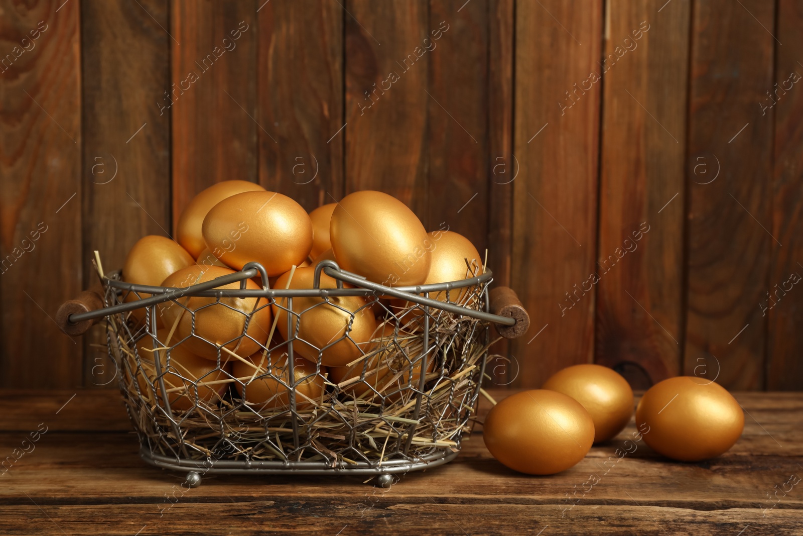 Photo of Shiny golden eggs in metal basket on wooden table