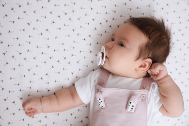 Photo of Cute little baby with pacifier lying on blanket, top view. Bedtime