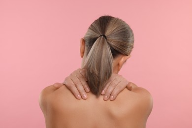 Photo of Woman suffering from pain in her neck on pink background, back view