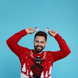 Photo of Happy young man in Christmas sweater and Santa headband on light blue background