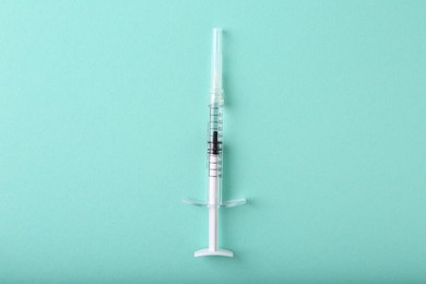 Photo of Cosmetology. Medical syringe on turquoise background, top view