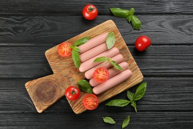 Photo of Fresh raw vegetarian sausages with basil and tomatoes on black wooden table, flat lay