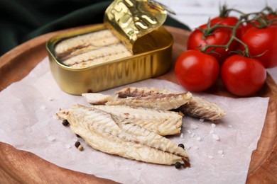 Photo of Delicious canned mackerel fillets and fresh tomatoes on wooden plate, closeup