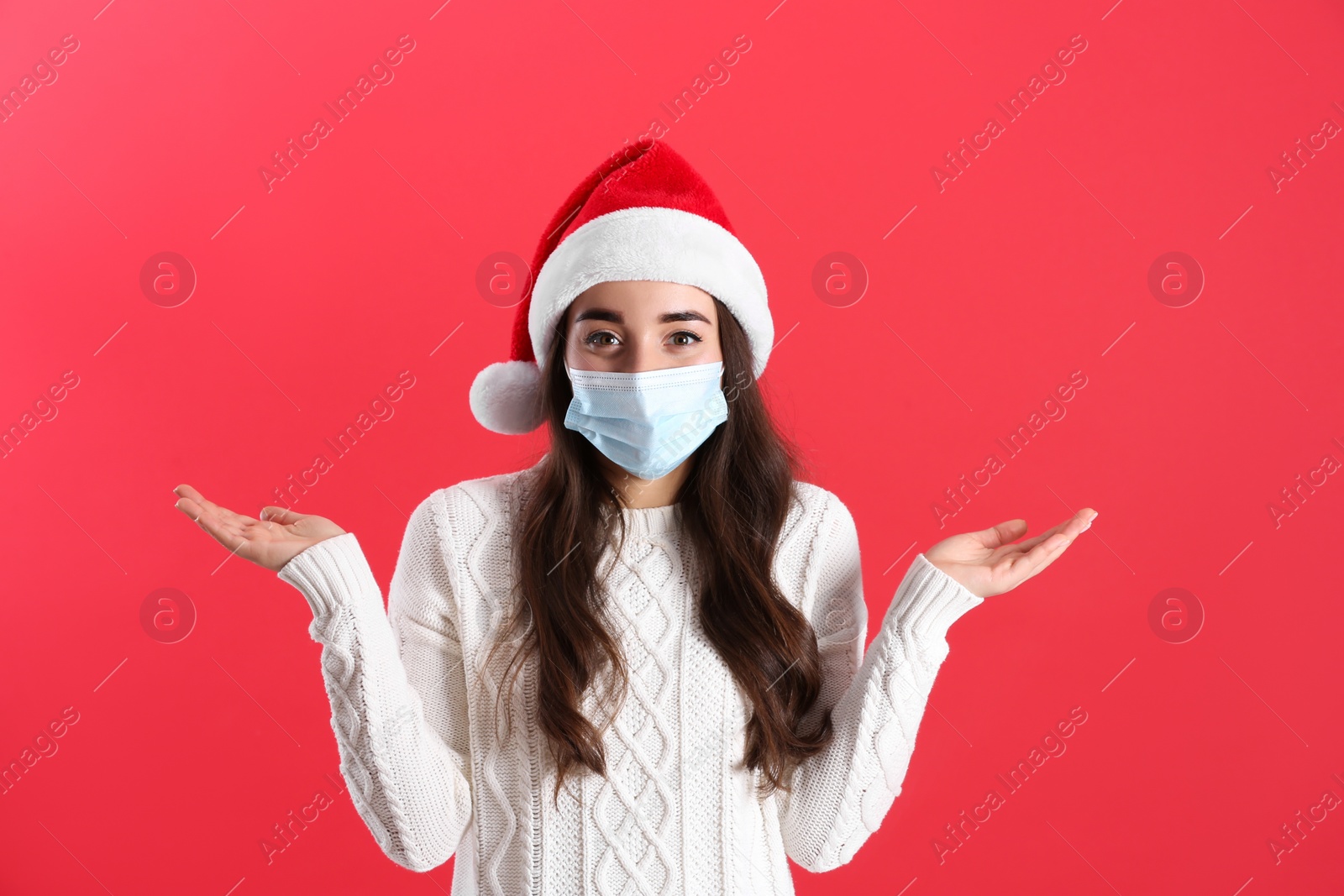 Photo of Beautiful woman wearing Santa Claus hat and medical mask on red background