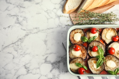 Flat lay composition with baked eggplant, tomatoes and basil in dishware on marble table. Space for text