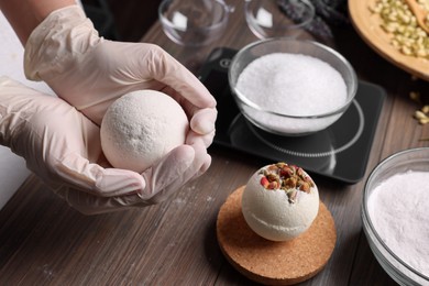Photo of Woman holding handmade bath bomb above wooden table, closeup