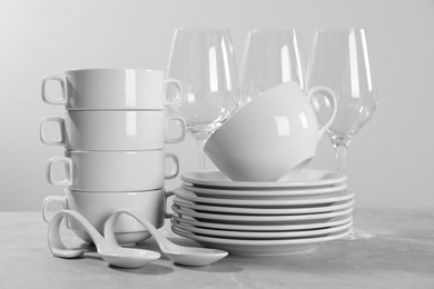 Photo of Set of clean dishware and glasses on grey table against light background