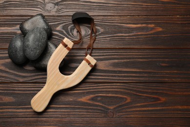 Photo of Slingshot with stones on wooden background, flat lay. Space for text