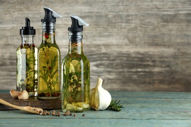 Photo of Cooking oil with different spices and herbs in bottles on wooden table. Space for text
