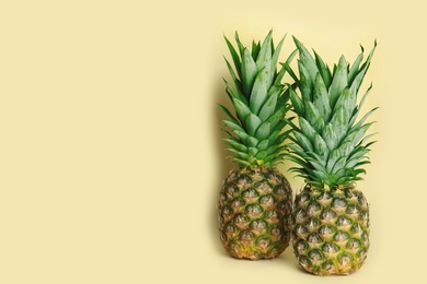 Photo of Ripe juicy pineapples on light yellow background. Space for text