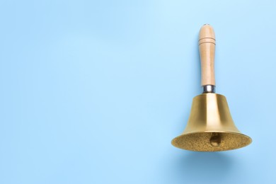 Photo of Golden school bell with wooden handle on light blue background, top view. Space for text