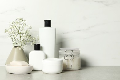 Photo of Bath accessories. Personal care products and gypsophila flowers in vase on gray table near white marble wall, space for text