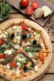 Tasty pizza with anchovies and ingredients on wooden table, flat lay
