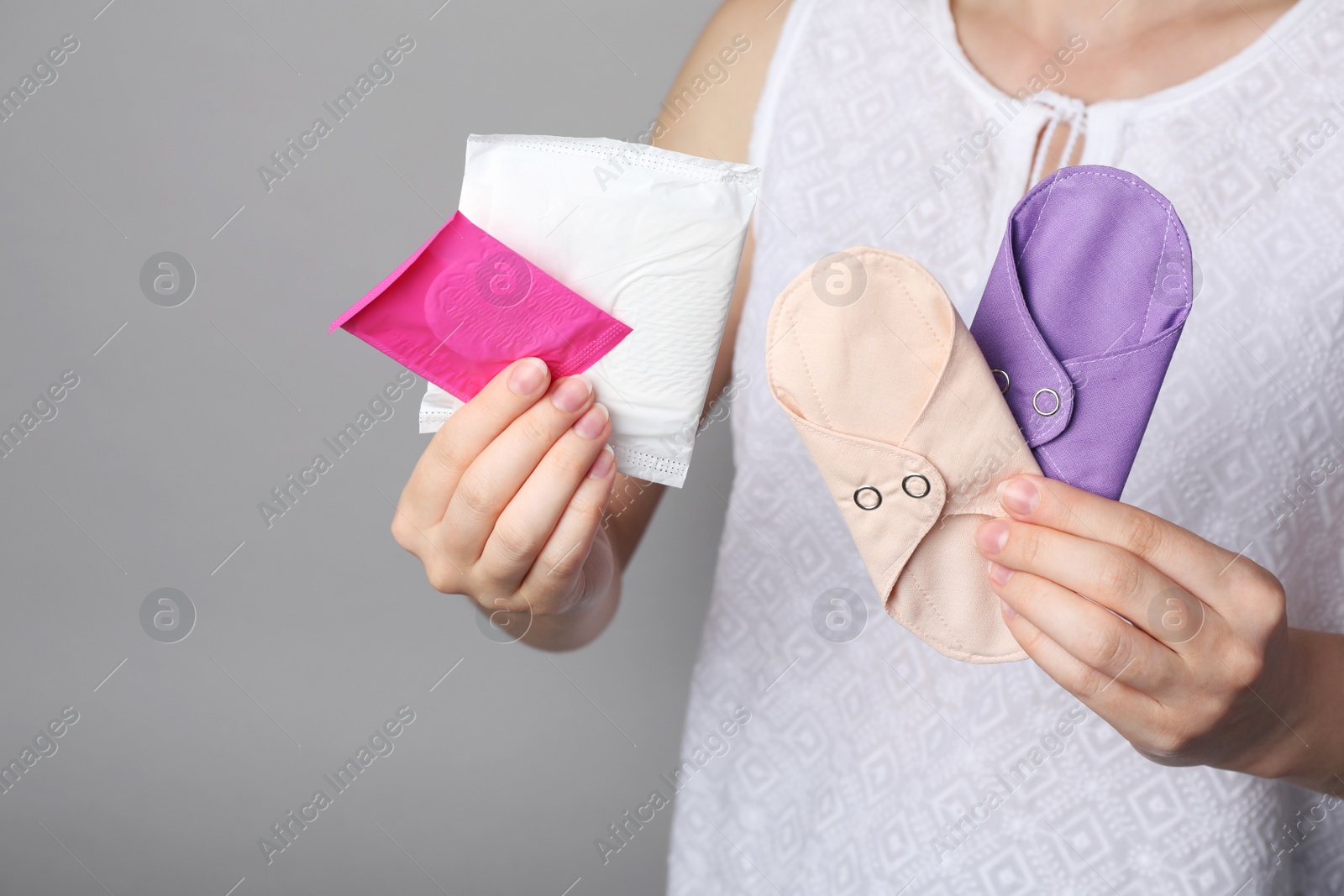 Photo of Woman holding disposable and reusable cloth menstrual pads on grey background, closeup