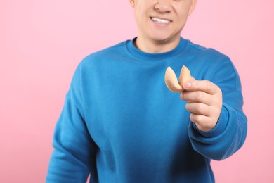 Photo of Happy man holding tasty fortune cookie with prediction on pink background, closeup