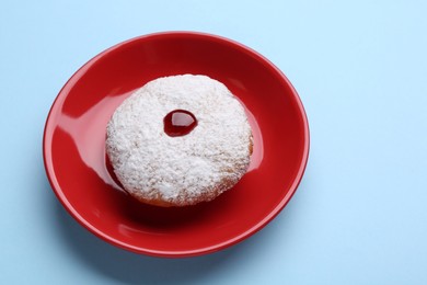 Photo of Hanukkah donut with jelly and powdered sugar on light blue background
