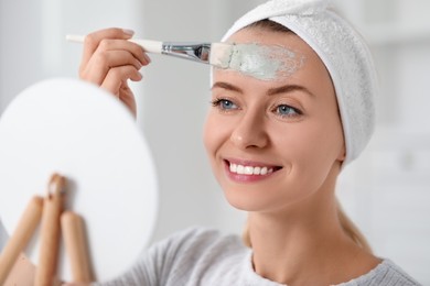 Photo of Young woman applying face mask in front of mirror indoors. Spa treatments