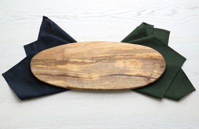 Photo of Empty wooden board and napkins on white table, top view