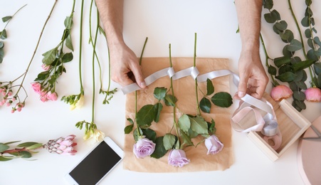 Male florist creating beautiful bouquet at table, top view