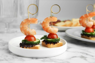 Photo of Tasty canapes with shrimps, cucumber, greens and tomatoes on white marble table, closeup