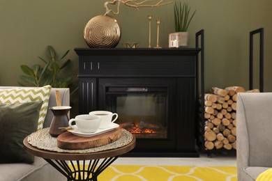 Photo of Cups of coffee and cezve on table near fireplace in living room
