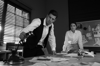 Photo of Old fashioned detective and his colleague working in office. Black and white effect