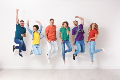 Photo of Group of young people in jeans and colorful t-shirts jumping near light wall