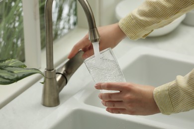 Photo of Woman filling glass with water from tap in kitchen, closeup