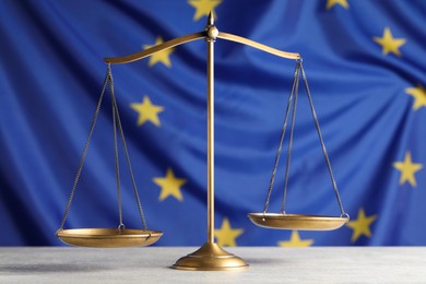 Photo of Scales of justice on light grey table against European Union flag