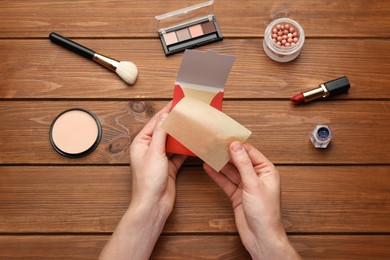 Photo of Woman with package of oil blotting tissues and decorative cosmetics at wooden table, top view. Mattifying wipes