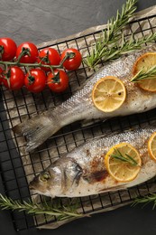 Photo of Baked fish with tomatoes, rosemary and lemon on black textured table, top view