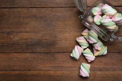 Photo of Glass jar with colorful marshmallows on wooden table, flat lay. Space for text
