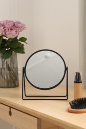 Photo of Mirror, foundation, brush and vase with pink roses on wooden dressing table in makeup room