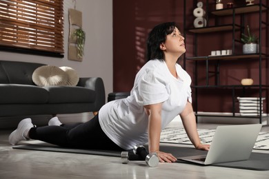 Photo of Overweight mature woman stretching while watching online class at home