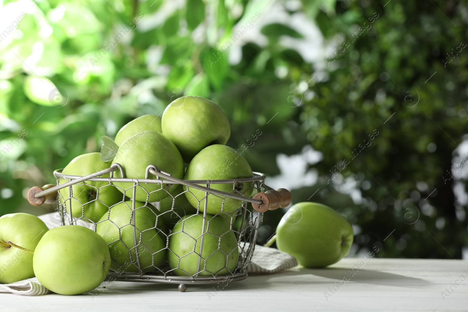 Photo of Metal basket with ripe green apples on white table outdoors, space for text