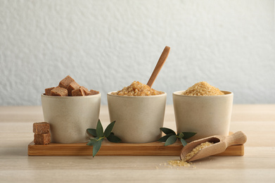 Photo of Bowls with different types of brown sugar on wooden table