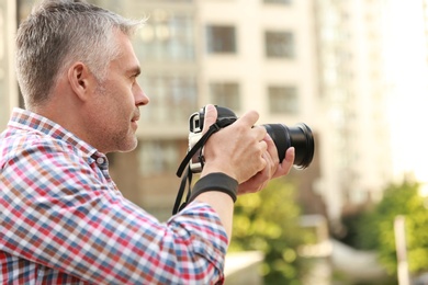 Photo of Handsome mature man taking photo with professional camera outdoors. Space for text