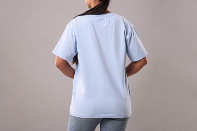 Photo of Woman wearing light blue t-shirt on grey background, closeup