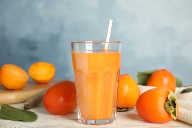 Photo of Fresh tasty persimmon smoothie and fresh fruits on white wooden table against light blue background