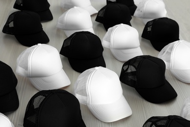 Photo of Many blank black and white caps on wooden table. Mock up for design