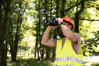 Photo of Forester with binoculars examining plants in forest, space for text