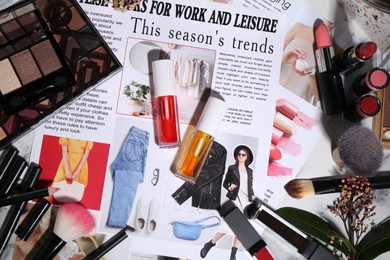 Photo of Bright lip glosses among different cosmetic products and fashion magazine on table, flat lay