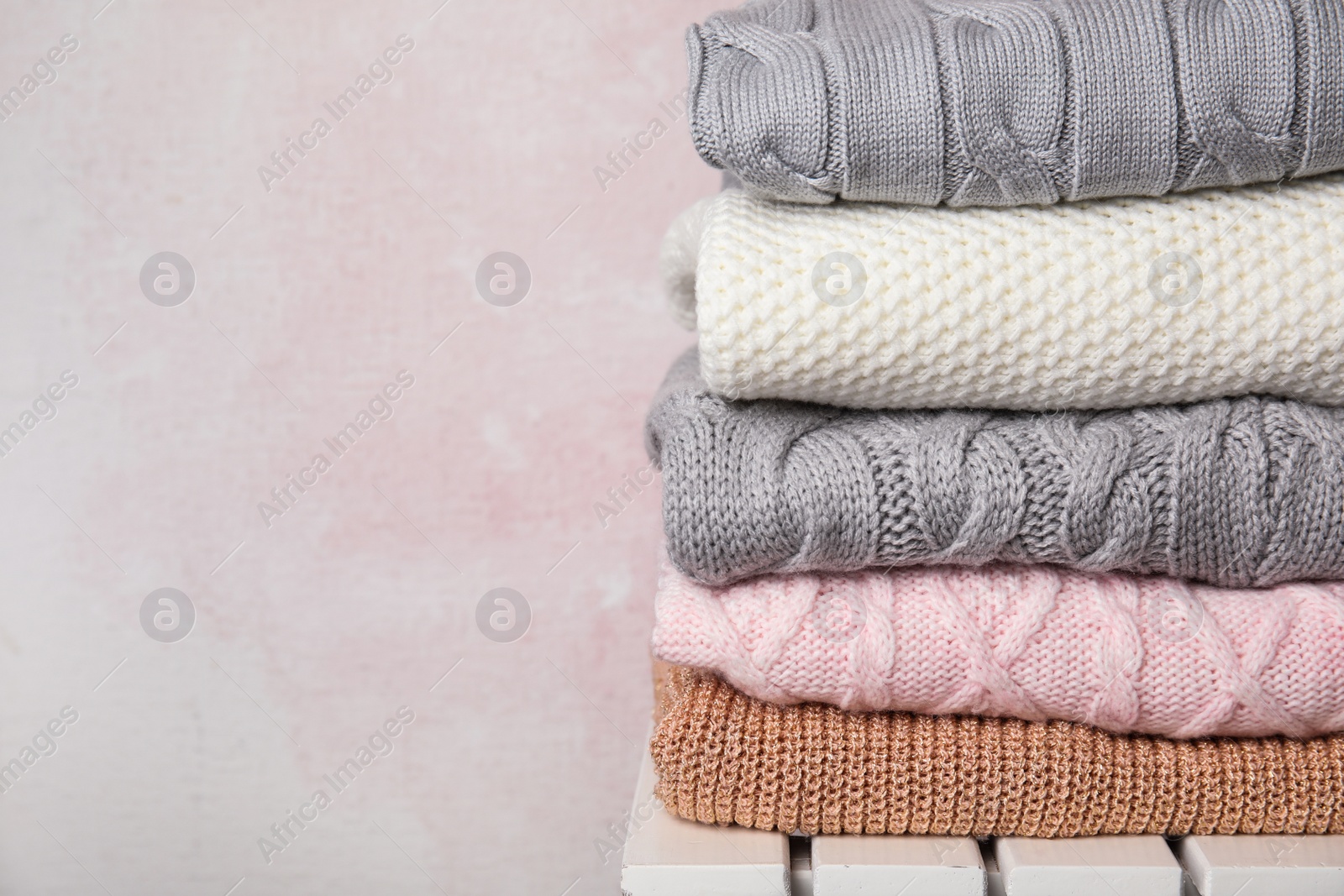 Photo of Stack of knitted clothes on white wooden table against pink background, space for text. Cozy autumn