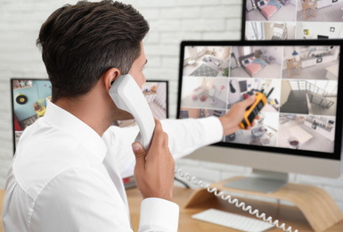 Photo of Male security guard talking by telephone near monitors at workplace