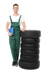 Photo of Young mechanic in uniform with car tires on white background