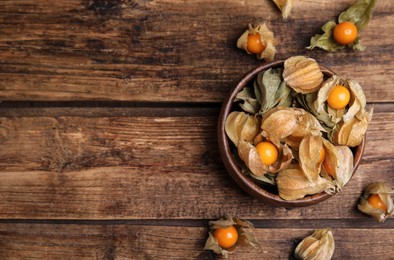 Photo of Ripe physalis fruits with dry husk on wooden table, flat lay. Space for text