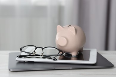Photo of Piggy bank, glasses, tablet and laptop on white table indoors