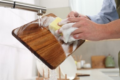 Photo of Man washing wooden cutting board in kitchen, closeup