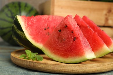 Photo of Slices of delicious ripe watermelon and mint on light blue wooden table, closeup